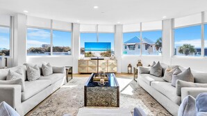 Un salon spacieux avec deux canapés, une table basse et une grande fenêtre donnant sur la plage et une maison.