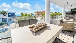 A modern outdoor dining area with a table and chairs, a decorative centerpiece, and a view of the ocean and buildings in the background. - The Viridian 201 (Santa Rosa Beach)