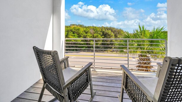 A balcony with two wicker chairs, a metal railing, and a view of a road and greenery. - The Viridian 201 (Santa Rosa Beach)