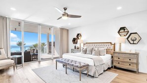 A bedroom with a large bed, a bedside table, a nightstand, a bench, and a view of the ocean through a sliding glass door. - The Viridian 201 (Santa Rosa Beach)