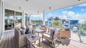Un balcon spacieux agrémenté de meubles en osier, une porte vitrée donnant sur un espace intérieur, et une vue sur un immeuble bleu et des palmiers.