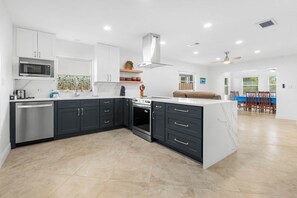 Een moderne keuken met donkere kastjes, een magnetron en een fornuis. Er is een eethoek met een tafel en stoelen.