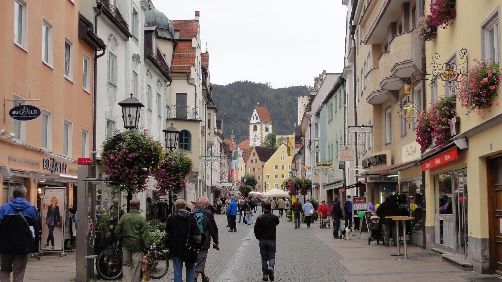 Eine Kopfsteinpflasterstraße gesäumt von historischen Gebäuden, einige mit Blumenkörben.