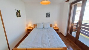 A bedroom with a wooden bed, two bedside lamps, and a large window with a view. - Stay at the slopes, stunning mountain views! (Le Grand-Bornand)