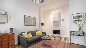 Ein modernes Wohnzimmer mit einem grauen Sofa, einem gemusterten Teppich, einer Holzkommode und einem schwarzen Konsolentisch mit einer Vase.