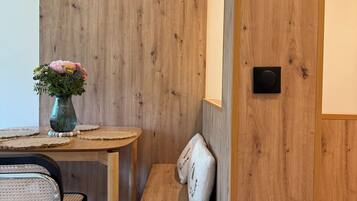 Una pared de madera, una pequeña mesa redonda con un florero, un banco y una silla.
