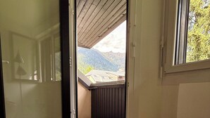 Une pièce dotée d’une porte coulissante donnant sur un balcon, d’un fauteuil en osier avec un coussin et d’une fenêtre offrant une vue sur les montagnes.