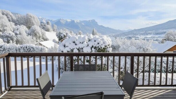A wooden deck with a table and chairs, overlooking a snowy landscape with trees and mountains. - Large family home near lake and resorts (Saint-André-d'Embrun)