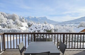 Una terraza de madera con mesa y sillas, con vistas a un paisaje nevado de árboles y montañas.