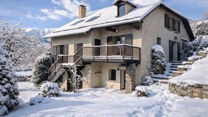 A two-story chalet with a balcony, stone foundation, and a snowy landscape. - Large family home near lake and resorts (Saint-André-d'Embrun)