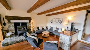 A cozy living room with a stone fireplace, wooden beams, a sofa set, and a stone accent wall. - Large family home near lake and resorts (Saint-André-d'Embrun)
