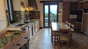 A kitchen with a foosball table, a dining table with chairs, and a view through a glass door. - Large family home near lake and resorts (Saint-André-d'Embrun)