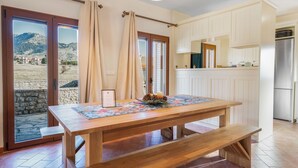 A wooden dining table with a placemat, benches, and a view of mountains through glass doors. - Anemos Mountain Villa - Your Perfect Mountain Retreat (Arachova)