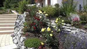 A garden with a variety of flowers and plants, a stone pathway, and a building with a wooden balcony.