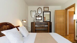 Ein Schlafzimmer mit einem hölzernen Bett, weißer Bettwäsche, einem Schminktisch und einem Spiegel.