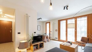 Ein modernes Wohnzimmer mit Flachbildfernseher, Couchtisch, Sofa und Essbereich mit Glastisch und Stühlen.