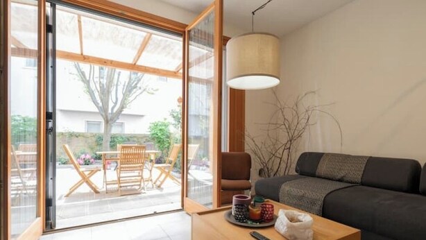 Ein modernes Wohnzimmer mit einer Couch, einem Couchtisch mit Fernbedienung sowie einem Essbereich mit Stühlen und Tisch.
