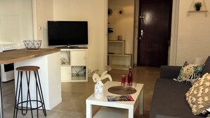 Een moderne woonkamer met een flatscreen televisie, een salontafel met decoratieve voorwerpen, een bank en een keukenhoek met een magnetron en een broodrooster.