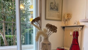 Een tafel met een geweven placemat, een vaas met gedroogde bloemen, een rode Coca-Cola blikje, een rode fles en twee glazen.
