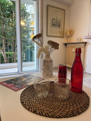 A table with a woven placemat, a vase with dried flowers, a red Coca-Cola can, a red bottle, and two glasses. - Cosy studio 10 min from Cannes (Le Cannet)