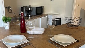 Een houten eettafel gedekt met witte borden, twee wijnglazen, een rode fles en een witte schaal.