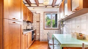 A compact kitchen with wooden cabinets, a dining table with chairs, and a window providing natural light. - Cà San Cosmo (Venezia)