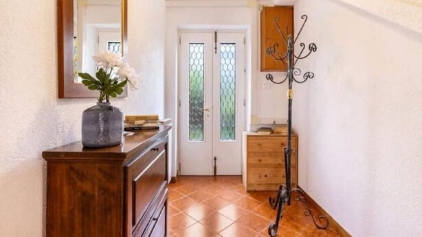 A hallway with a wooden dresser, a mirror, a vase with flowers, a coat rack, and a door with glass panels. - Cà San Cosmo (Venezia)