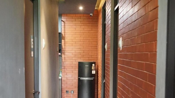 A corridor with a brick wall on one side and a plain wall on the other, leading to a black refrigerator. - Rizki Kost Exclusive II (Depok)
