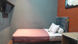 A single bed with a pink bedspread and white pillows, a small desk with a computer, and a wall-mounted television. - Rizki Kost Exclusive II (Depok)