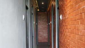 A corridor with a grey tiled floor, red brick walls, and doors with light switches. - Rizki Kost Exclusive II (Depok)