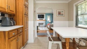 Une cuisine avec des meubles en bois, une machine à café et un coin repas comprenant une table et des chaises blanches.