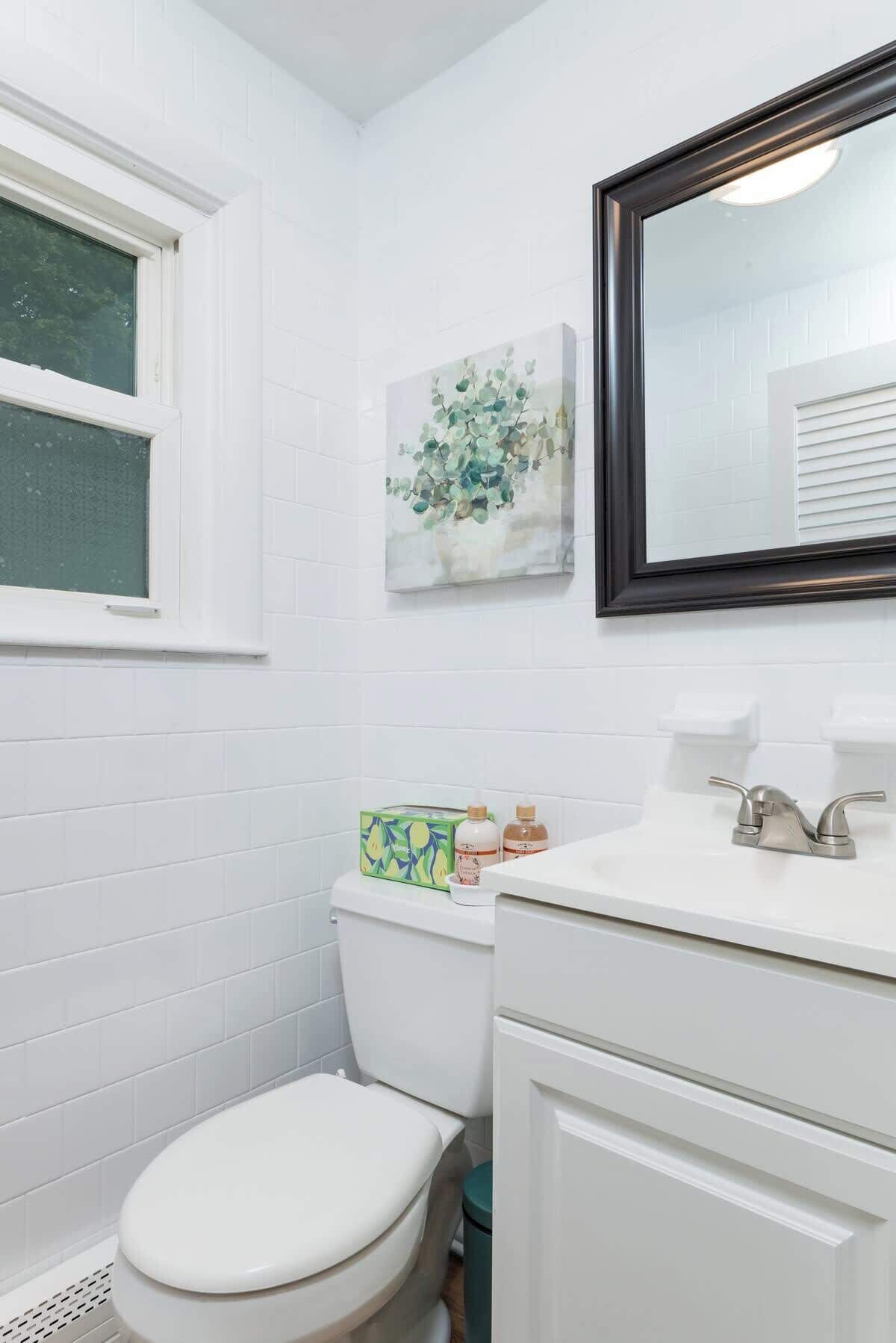 A bathroom with a white toilet, a sink with a mirror above it, and a window.