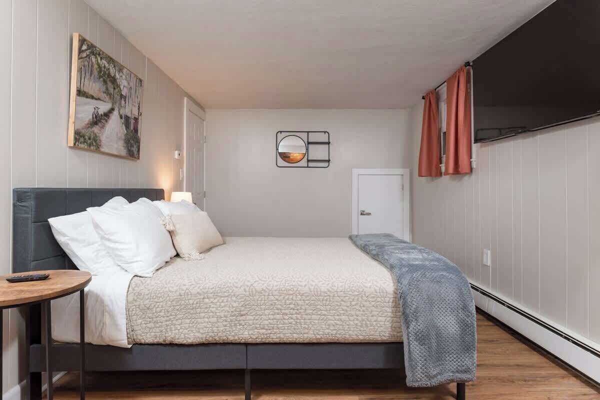 Ein Schlafzimmer mit einem Bett, einem Nachttisch, einem Wandspiegel, einer Tür und einem Fenster mit Vorhängen.