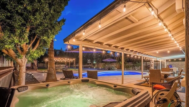 A hot tub area with a covered patio, lounge chairs, and a pool in the background. - Backyard Paradise in Chandler (Chandler)