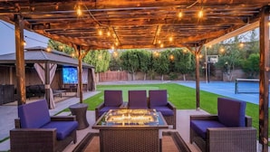 An outdoor patio with wicker furniture, a glass-top table, and string lights. - Backyard Paradise in Chandler (Chandler)