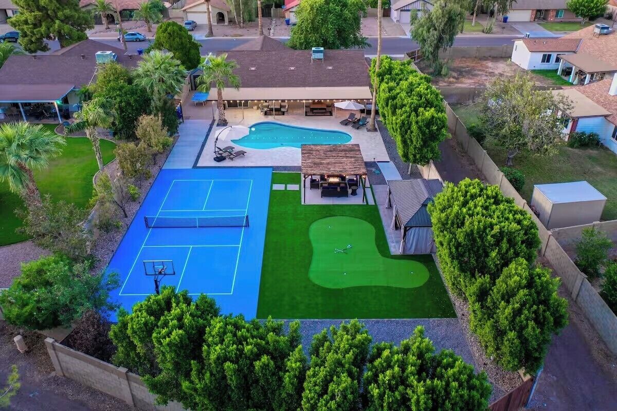 A residential backyard with a swimming pool, tennis court, and a small putting green.