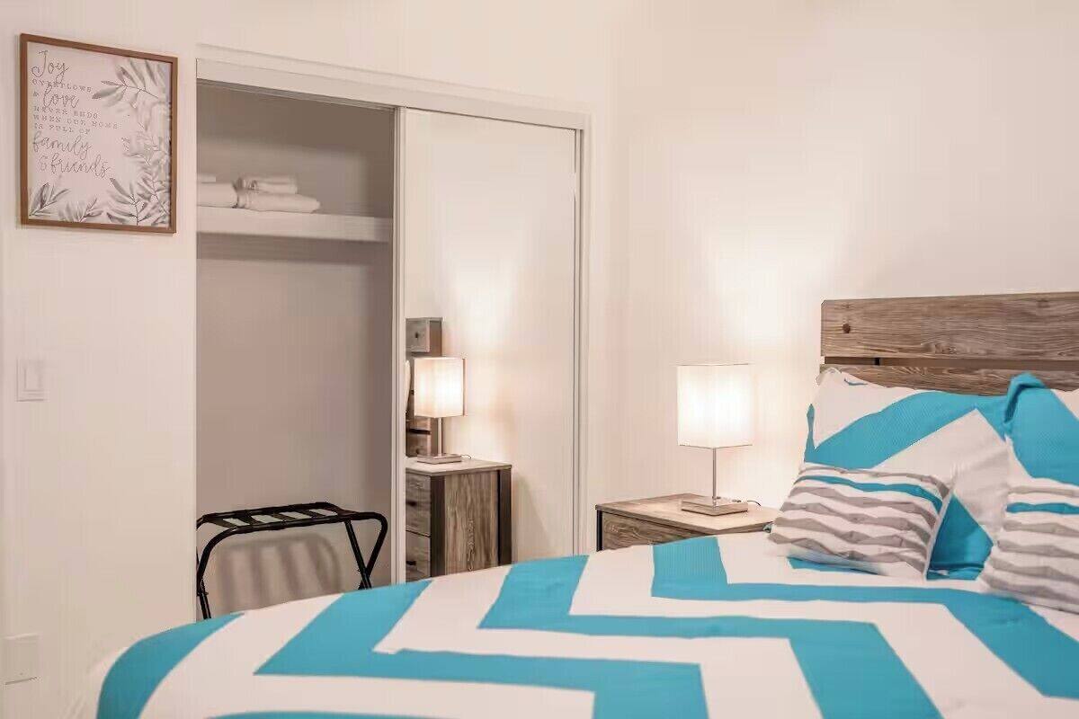A hotel room with a bed, a nightstand, a lamp, a wardrobe, and a framed quote on the wall.