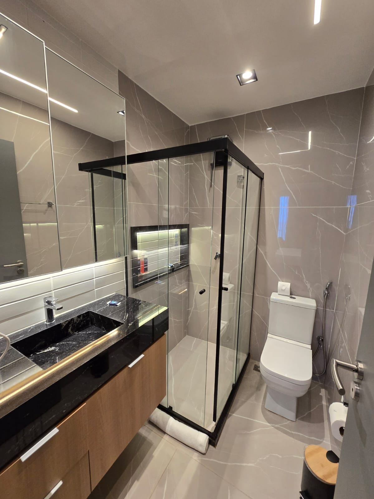 Un baño moderno con ducha envuelta en vidrio, inodoro y tocador con lavamanos.