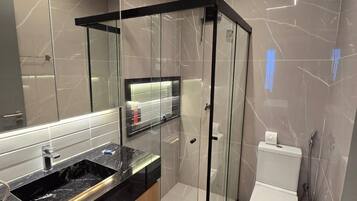 Un baño moderno con ducha envuelta en vidrio, inodoro y tocador con lavamanos.