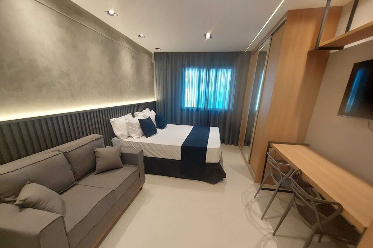 Moderni hotellihuone, jossa on sänky, sohva, työpöytä ja televisio.