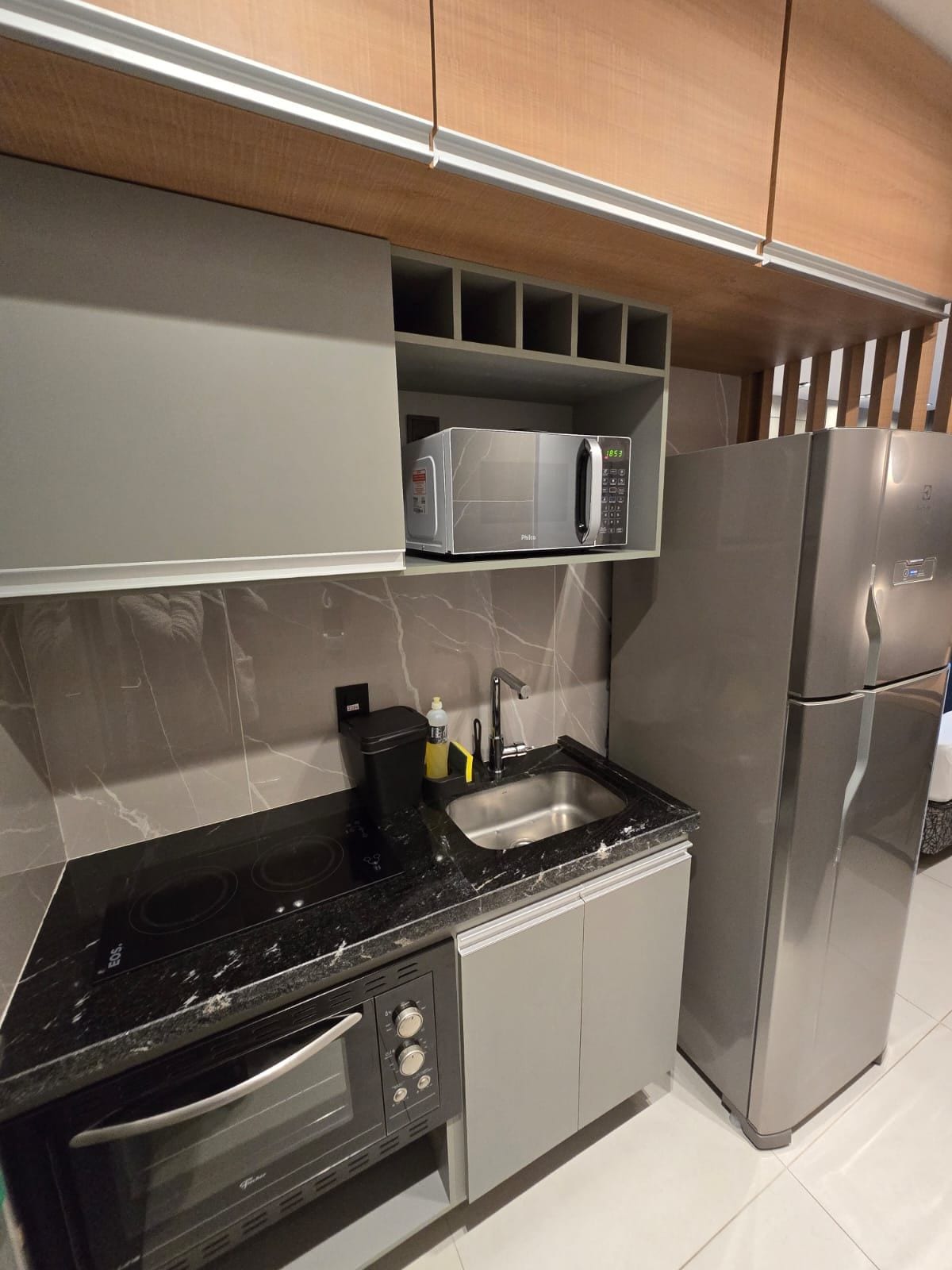 A modern kitchen with a built-in microwave, stainless steel refrigerator, and a black countertop.
