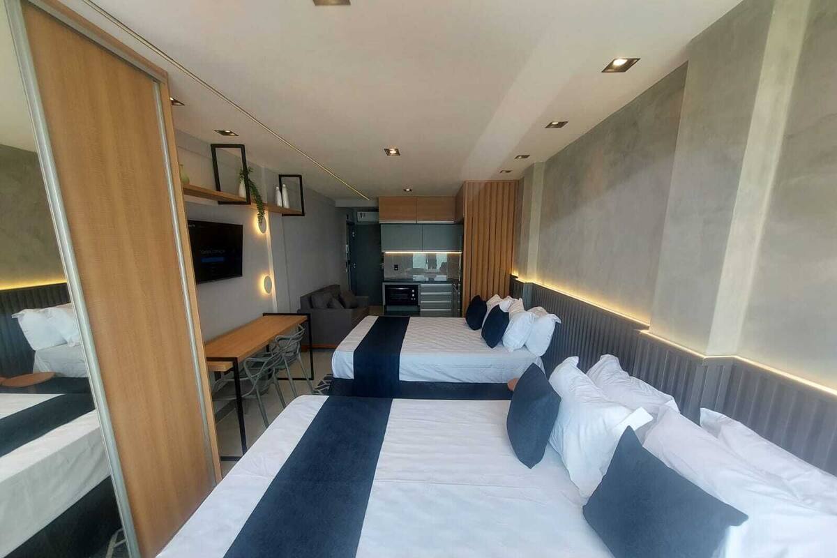 Habitación de hotel con dos camas, un escritorio, una silla, un televisor y una kitchenette.