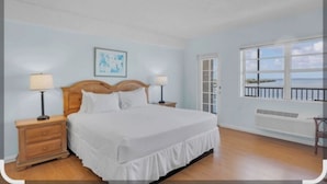 A bedroom with a wooden bed, two bedside tables with lamps, a window with a view of the sea, and a ceiling fan. - Key Largo Waterfront 1 bedroom condo. (Key Largo)