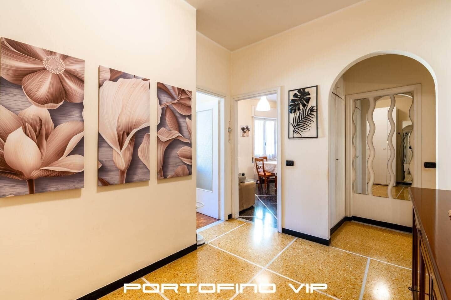 Un corridoio con pavimento piastrellato, un'area pranzo sullo sfondo e tre opere d'arte floreali alle pareti.