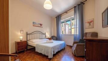 A bedroom with a bed, bedside table, lamp, and a view of the outside through a window.