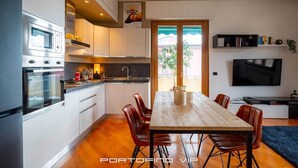 Een moderne keuken met inbouwapparatuur, een eethoek met een houten tafel en lederen stoelen, en een aan de muur bevestigde televisie.