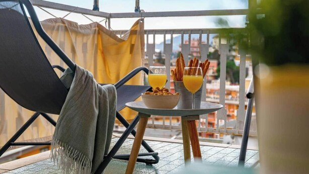 Een balkon met een stoel, een tafeltje en een kom cornflakes met een glas jus d'orange.