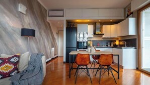 Een moderne keuken met een centraal eiland, ingebouwde apparatuur en een eethoek met een houten tafel en twee stoelen.