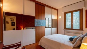 Een slaapkamer met een bed, een stoel, een bureau en een raam met zonwering.