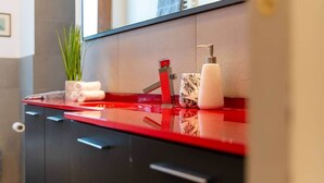 Een moderne badkamer met een rode countertop, een rode kraan, een witte zeepdispenser en een potplant.